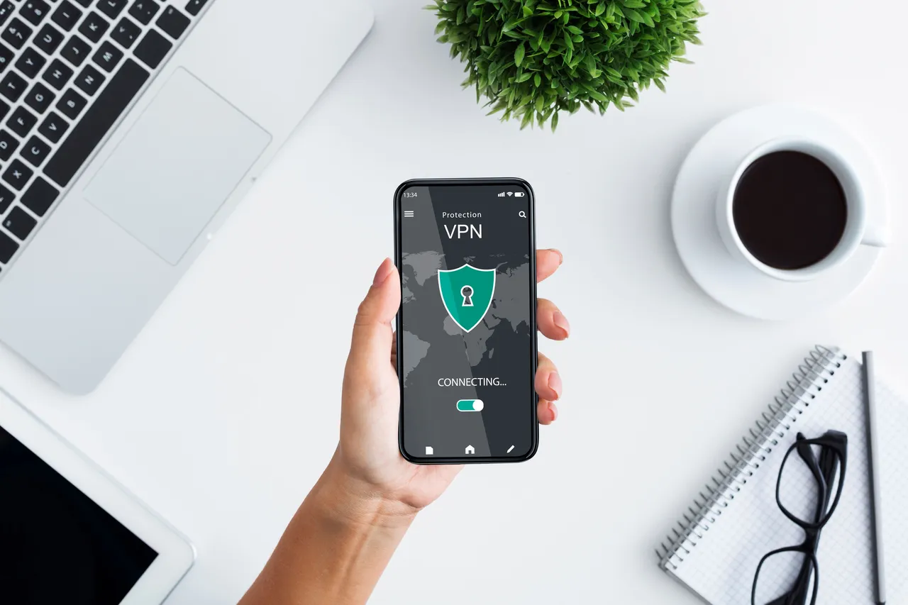 Osoba trzyma w dłoni włączonego smartfona, który łączy się z serwerem VPN, by zyskać bezpieczny dostęp do internetu.